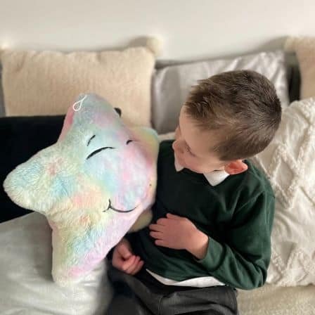 Young boy sitting on a couch, smiling and holding a plush pastel-colored sensory star with a happy face, creating a calming and comforting moment.